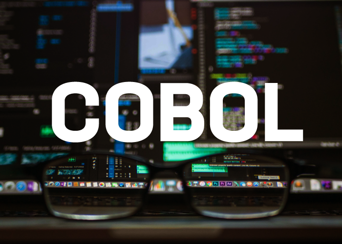 text saying cobol and background is a table with computer screens with programming environment and a pair of black glasses